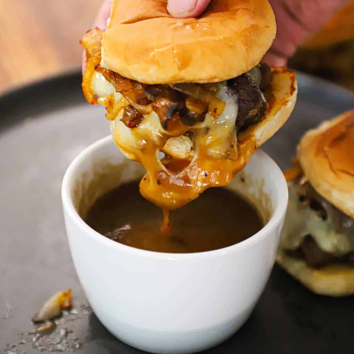 A person raising a pot roast slider out of a small bowl filled with grown gravy.