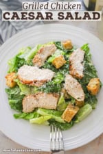 A white dinner plate filled with grilled chicken Caesar salad with a glass of white wine next to it.