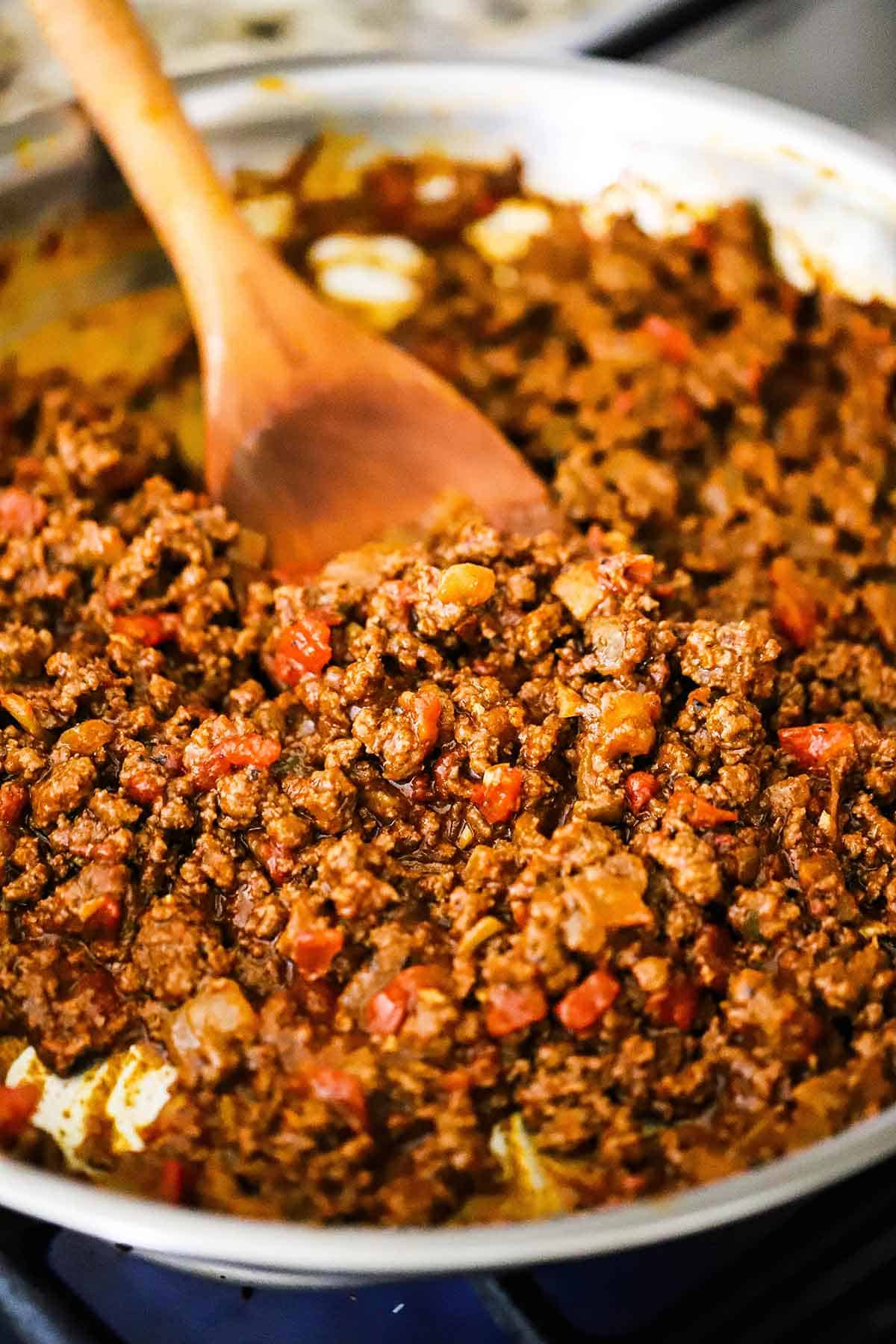 A large silver skillet filled with homemade beef taco meat made with homemade taco seasoning with a wooden spoon inserted off to the side.