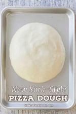 A partially risen ball of New York-style pizza dough on a silver metal sheet pan.