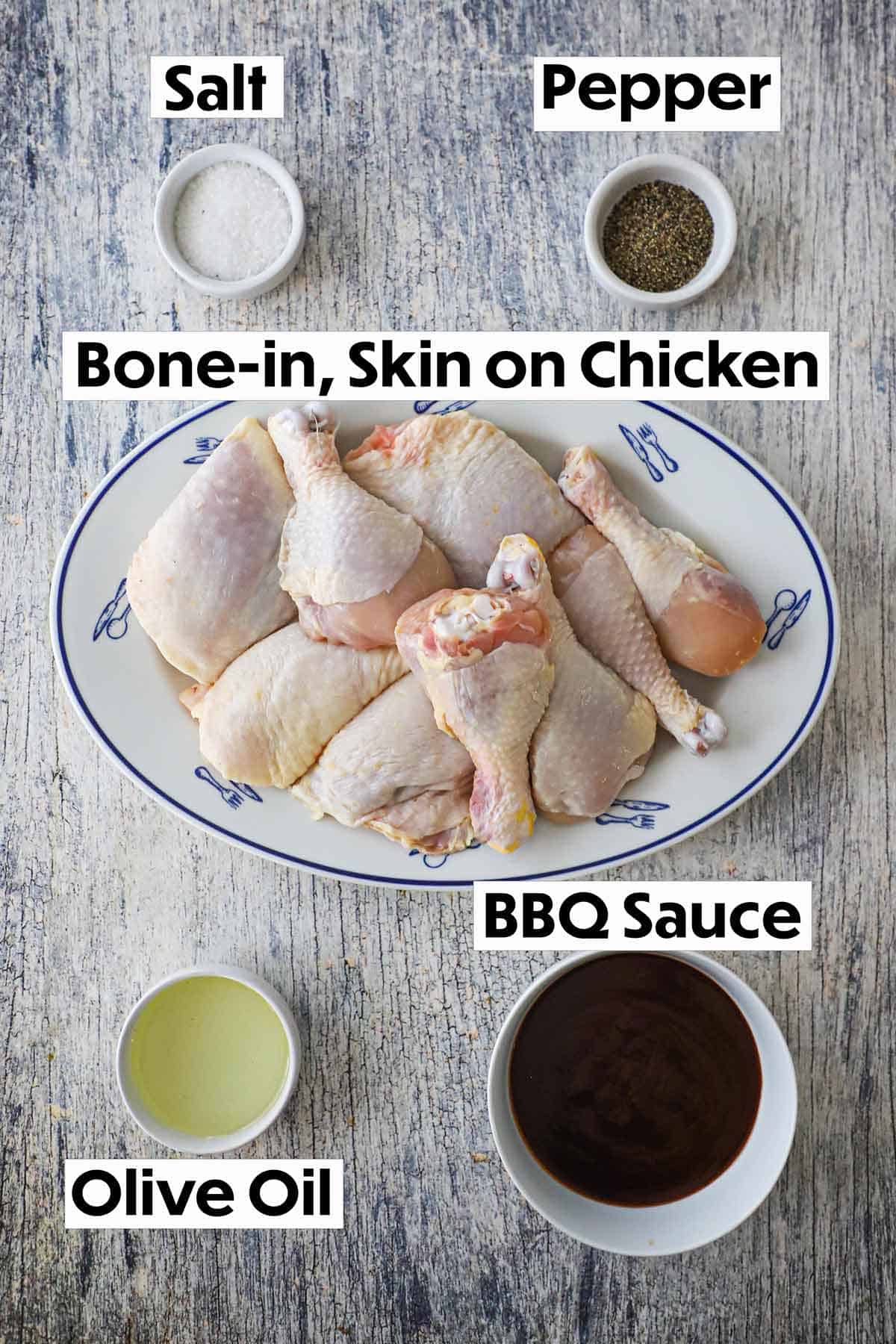 An arrangement of ingredients for grilled BBQ chicken on a grey wooden background including uncooked chicken pieces, salt, pepper, olive oil, and BBQ sauce.
