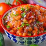 A close-up view of a colorful bowl of filled with a pile freshly made pico de gallo with chopped tomatoes, red onion, jalapeño, and cilantro.