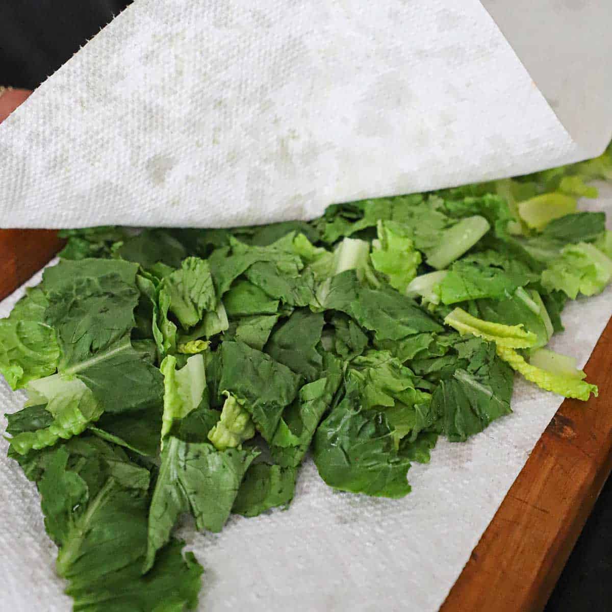 A person using several pieces of paper towels to dry chopped Romaine lettuce that has been rinsed with water.