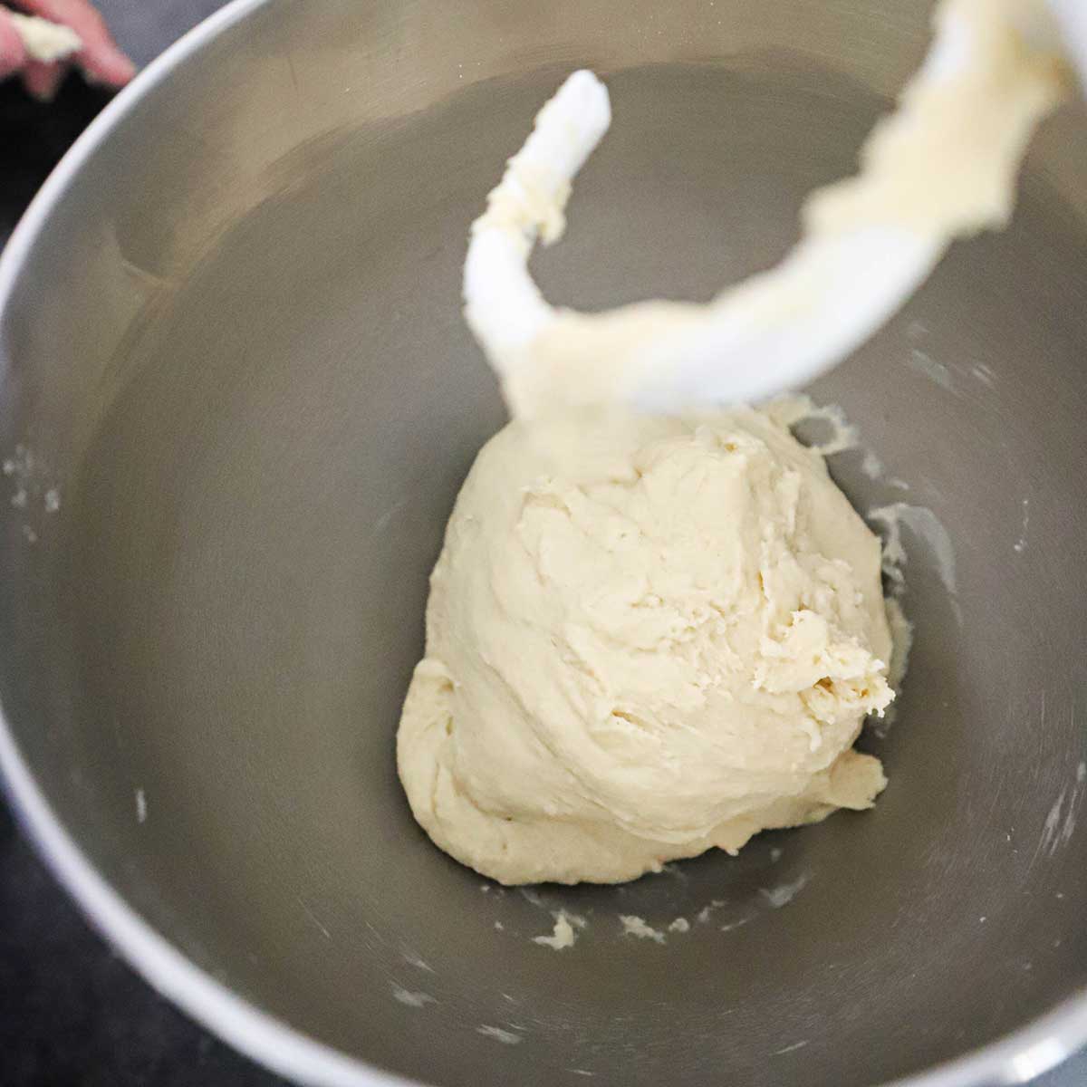 A ball of hamburger dough that has just been kneaded with a dough hook in the bowl of a stand mixer.