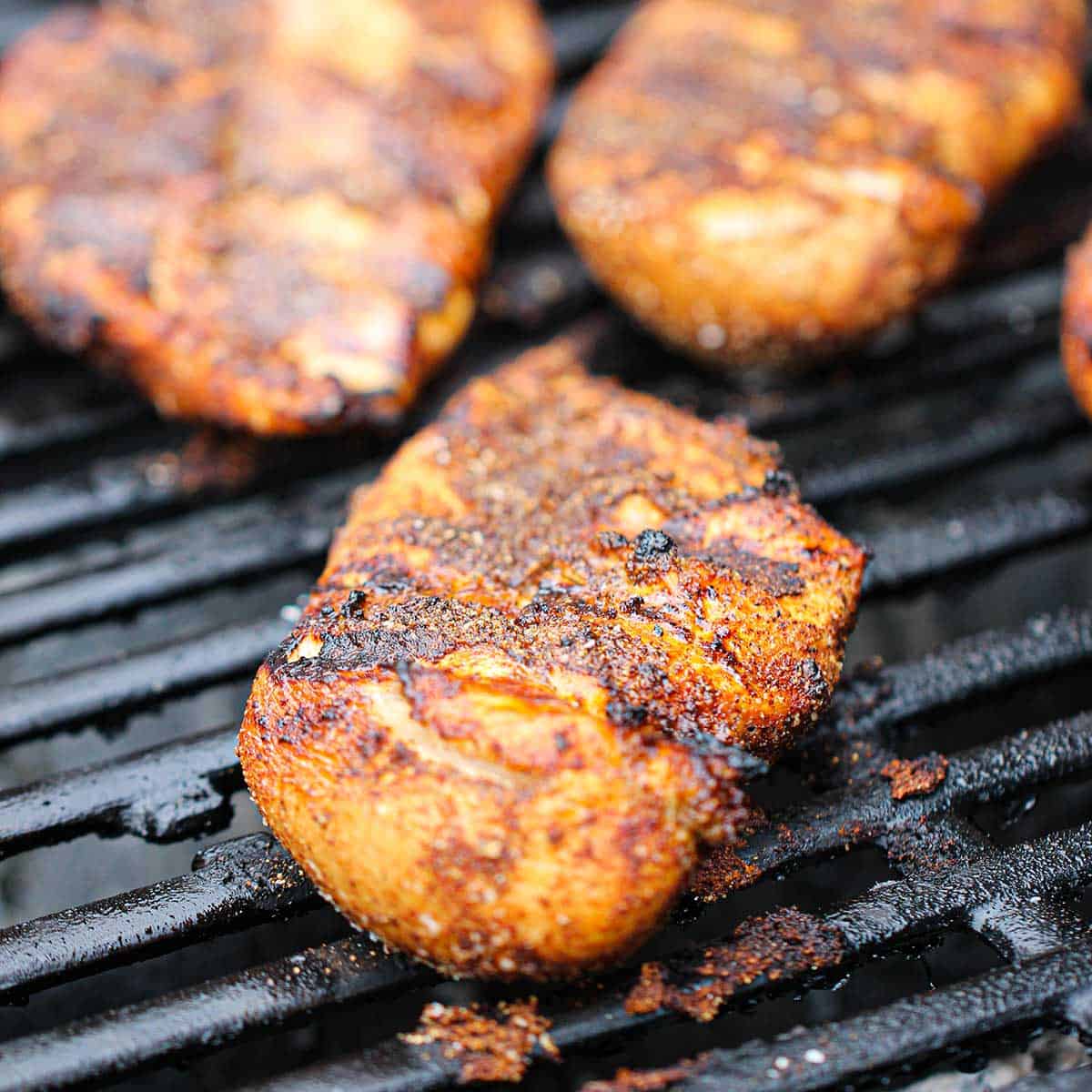 Seasoned skinless chicken breast being grilled on a gas grill and have visible grill marks.