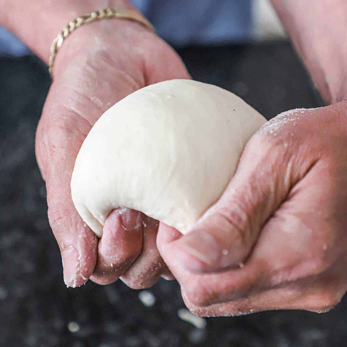 A person using his hands to smooth a round piece of New York-style pizza dough.