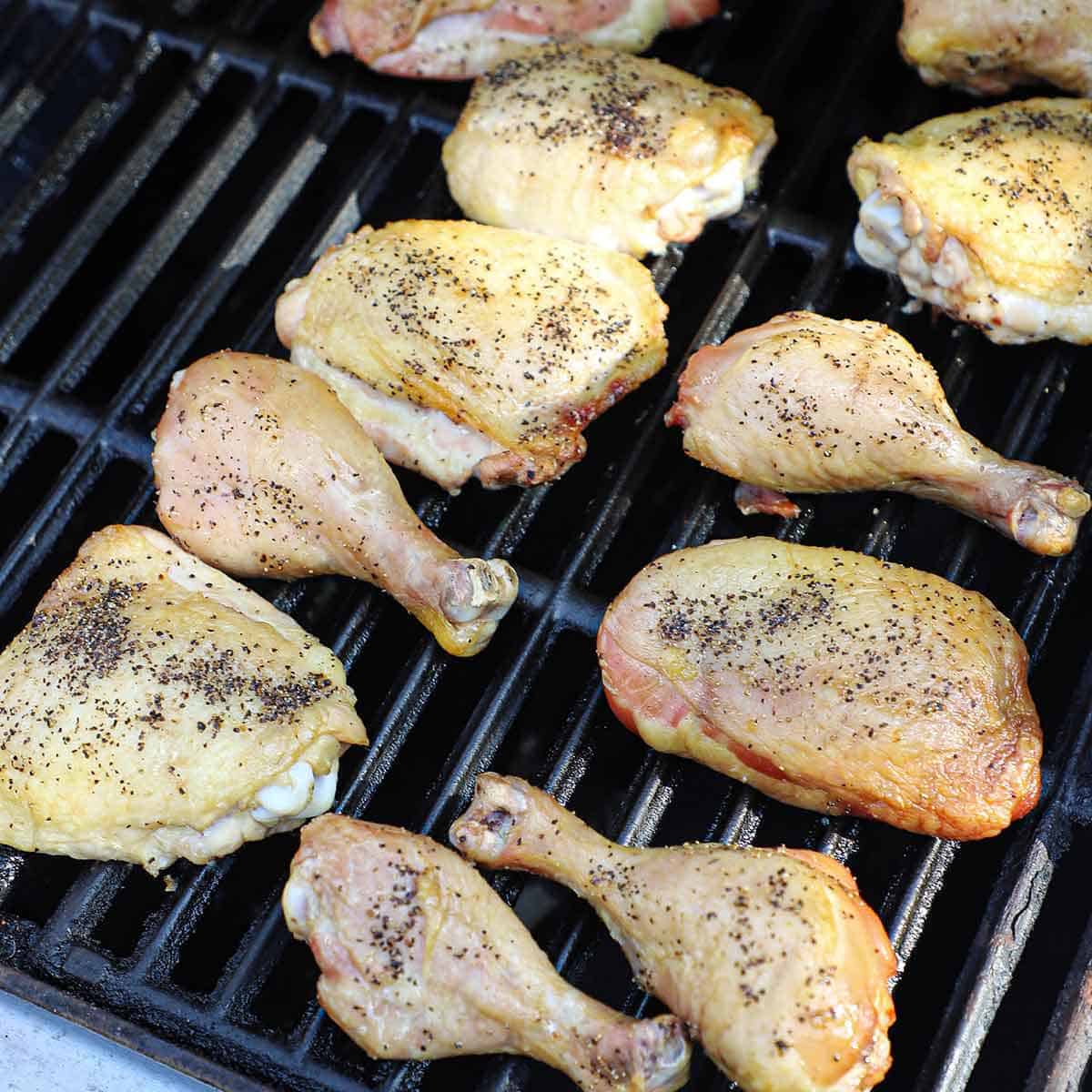 Seasoned chicken legs and chicken thighs grilling on a gas grill.
