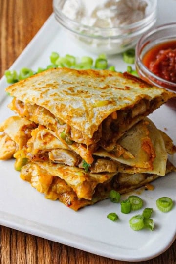 Three chicken quesadilla triangles sitting on top of each other on a white plate.