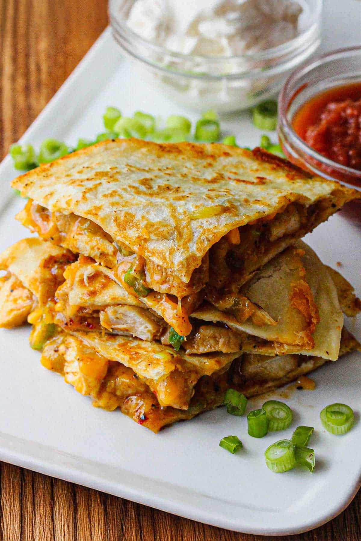 Three chicken quesadilla triangles sitting on top of each other on a white plate.