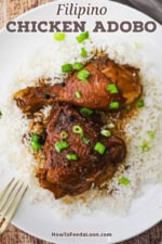 A serving of Filipino chicken adobo including a chicken leg and thigh resting on a bed of steamed white rice and garnished with chopped scallions all on a white dinner plate.