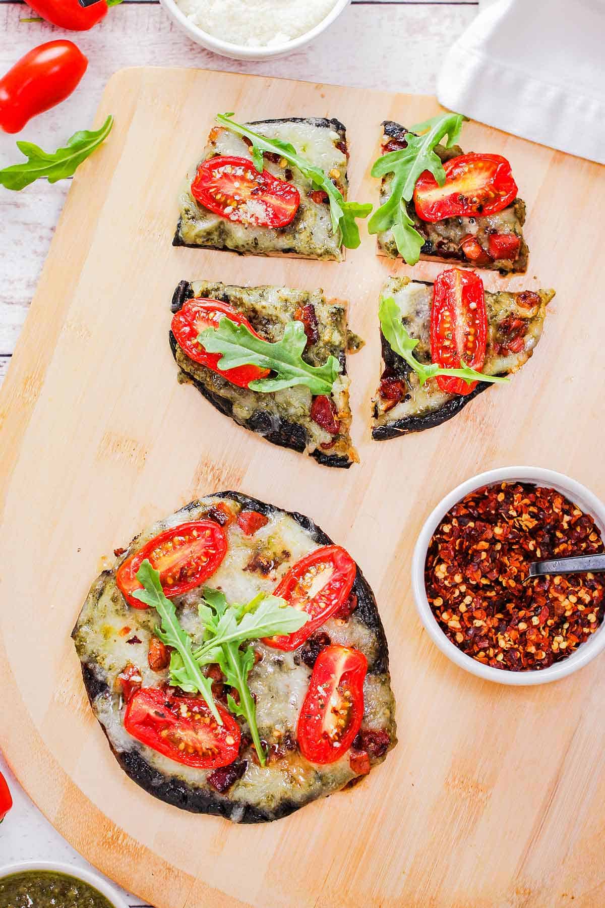 Two portobello BLT pizzas resting on a large pizza peel with one pizza cut into quarters and the other left whole.
