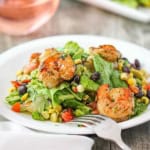 A white salad plate filled with a serving of grilled shrimp salad with cilantro-lime dressing with a stemless glass of rosé wine nearby.