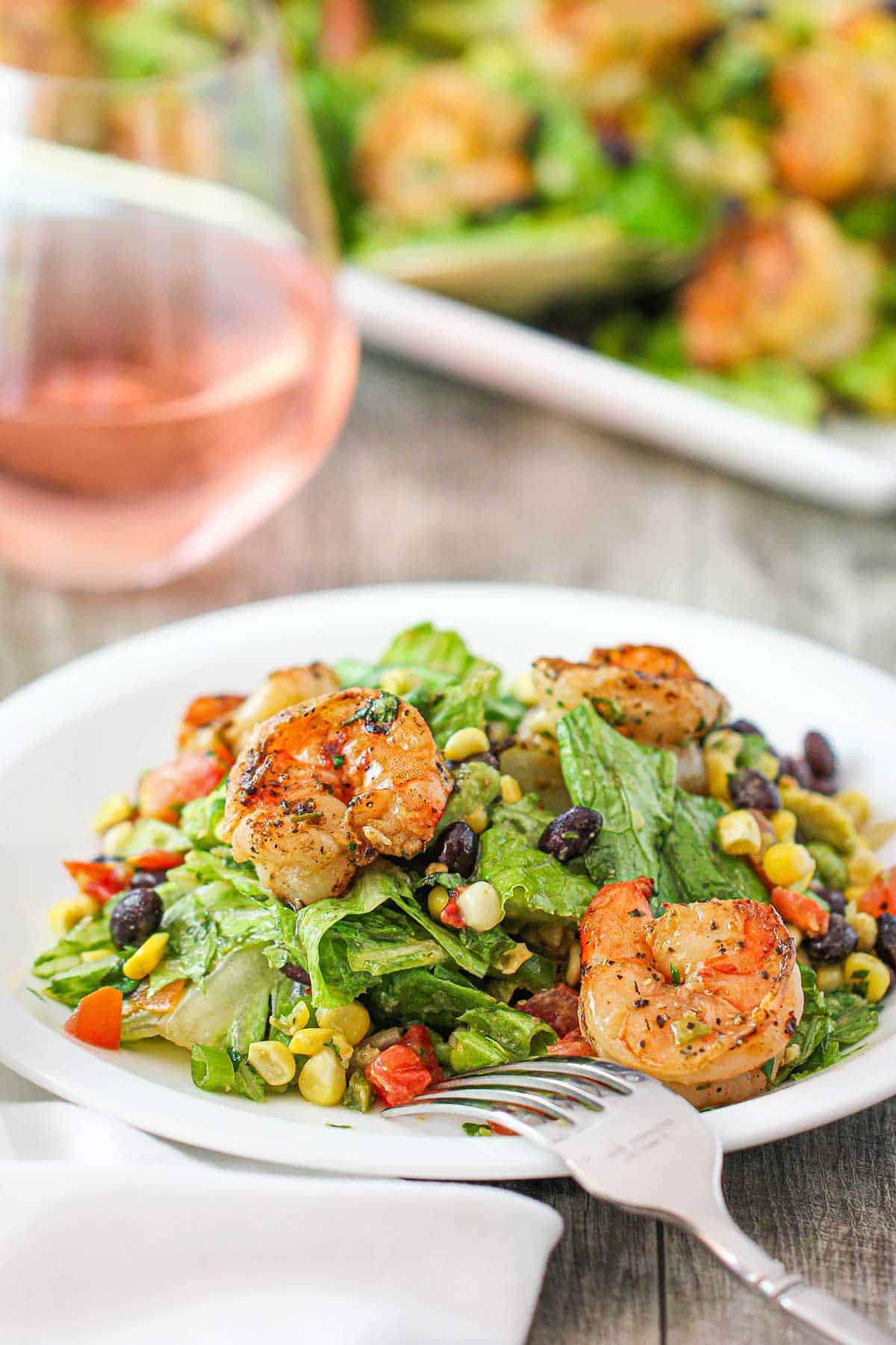 A white salad plate filled with a serving of grilled shrimp salad with cilantro-lime dressing with a stemless glass of rosé wine nearby.