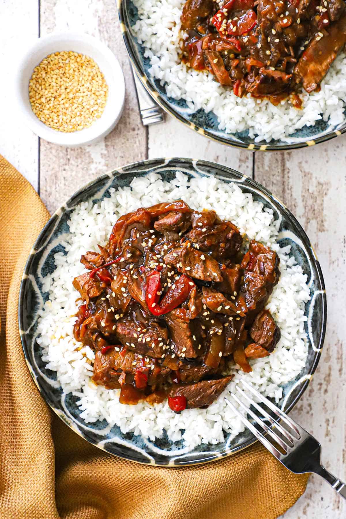 An overhead view of two shallow bowls filled with servings of slow cooker pepper steak and steamed white rice. 