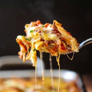 A person raising a cheesy serving of best-ever baked ziti from a pan of the same thing.