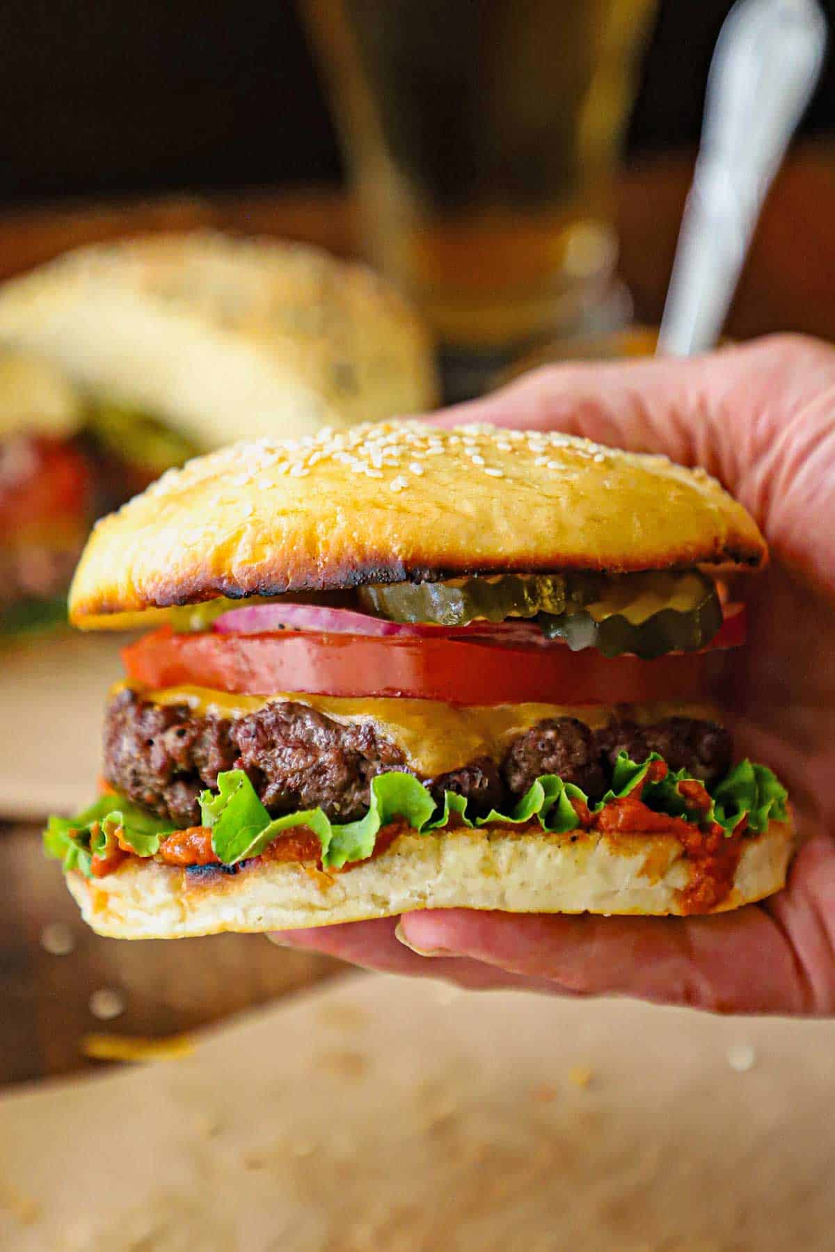 A person holding a best-ever cheeseburger consisting of a juicy beef burger topped with melting cheddar cheese, lettuce, tomato, red onion, and pickles all sandwiched between a toasted homemade hamburger bun.