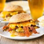 A grilled honey mustard chicken sandwich with bacon on a sesame seed bun sitting on a withe dinner plate with a frosty glass of beer in the background.