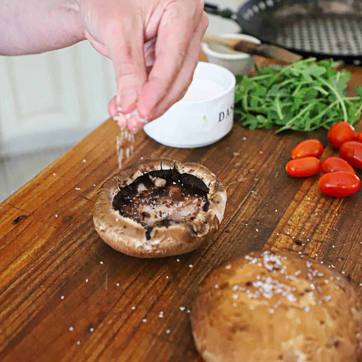 A person sprinkling Kosher salt on the inside of a large portobello mushroom cap that has had the internal gills removed.