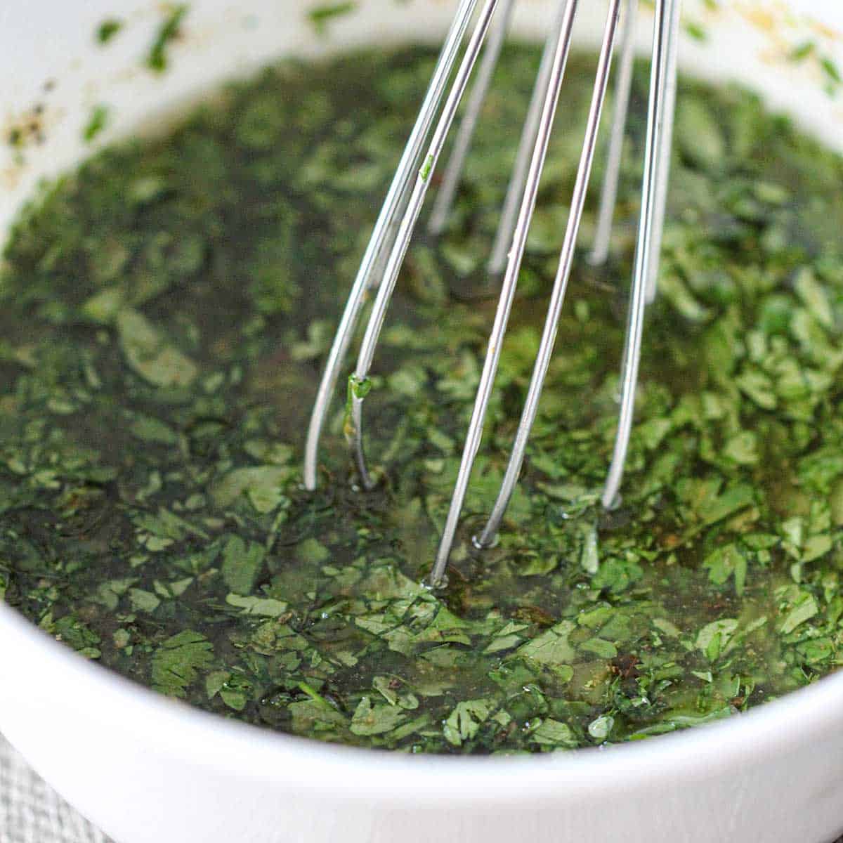 A close-up view of a whisk being used to whisk a cilantro-lime dressing in a small white bowl.