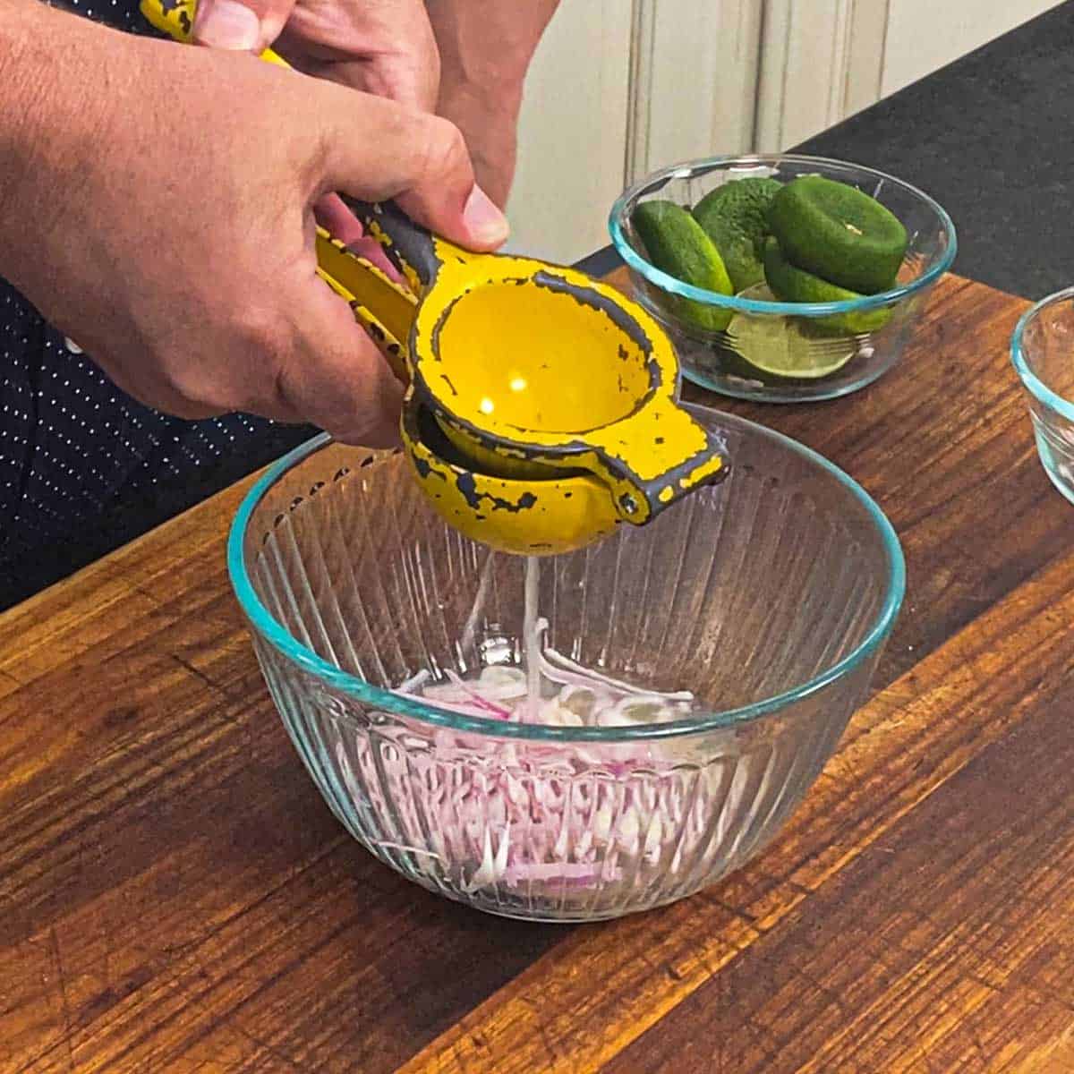 A person using a citrus juicer to squeeze fresh lime juice into a glass bowl filled with strips of shallot.