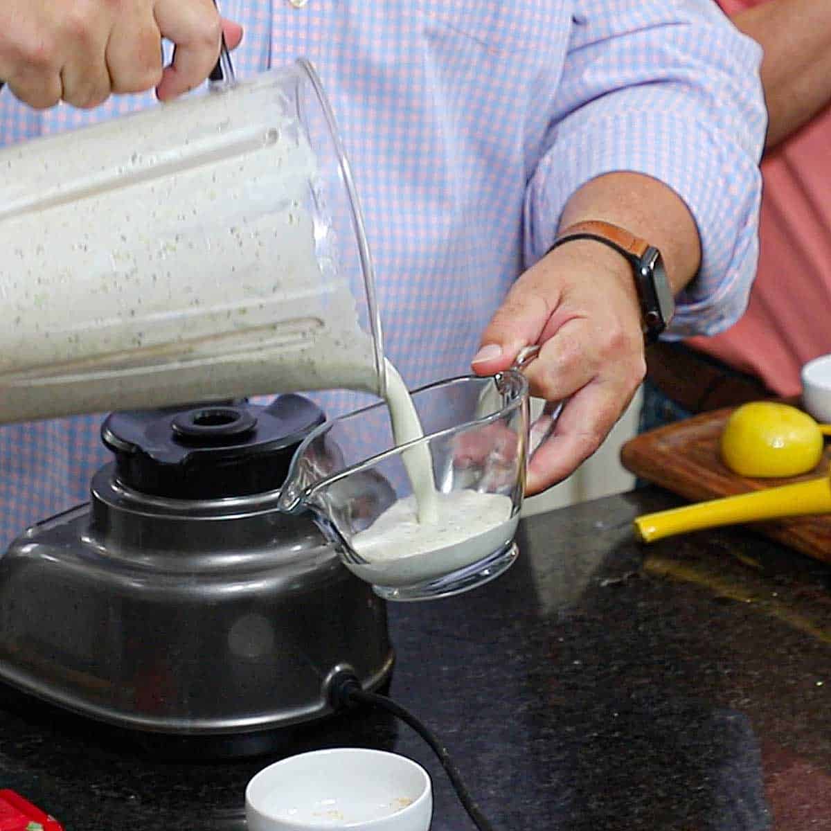 A person pouring a freshly puréed scallion buttermilk dressing from a blender into a glass gravy boat.