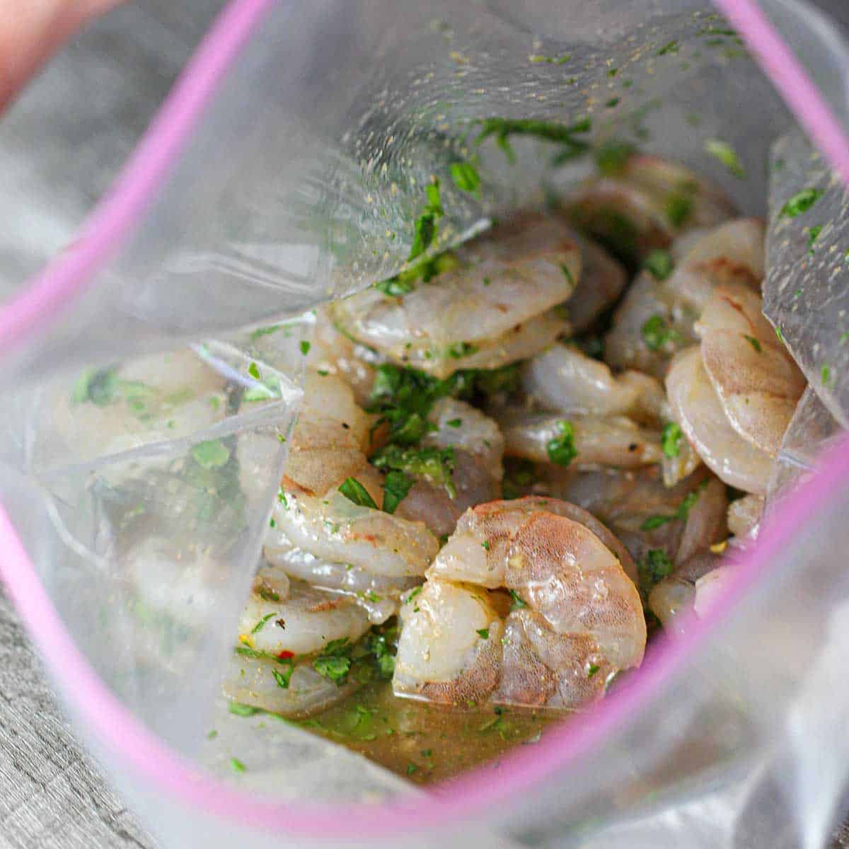 Uncooked shrimp piled inside a clear freezer bag also filled with a cilantro-lime marinade.