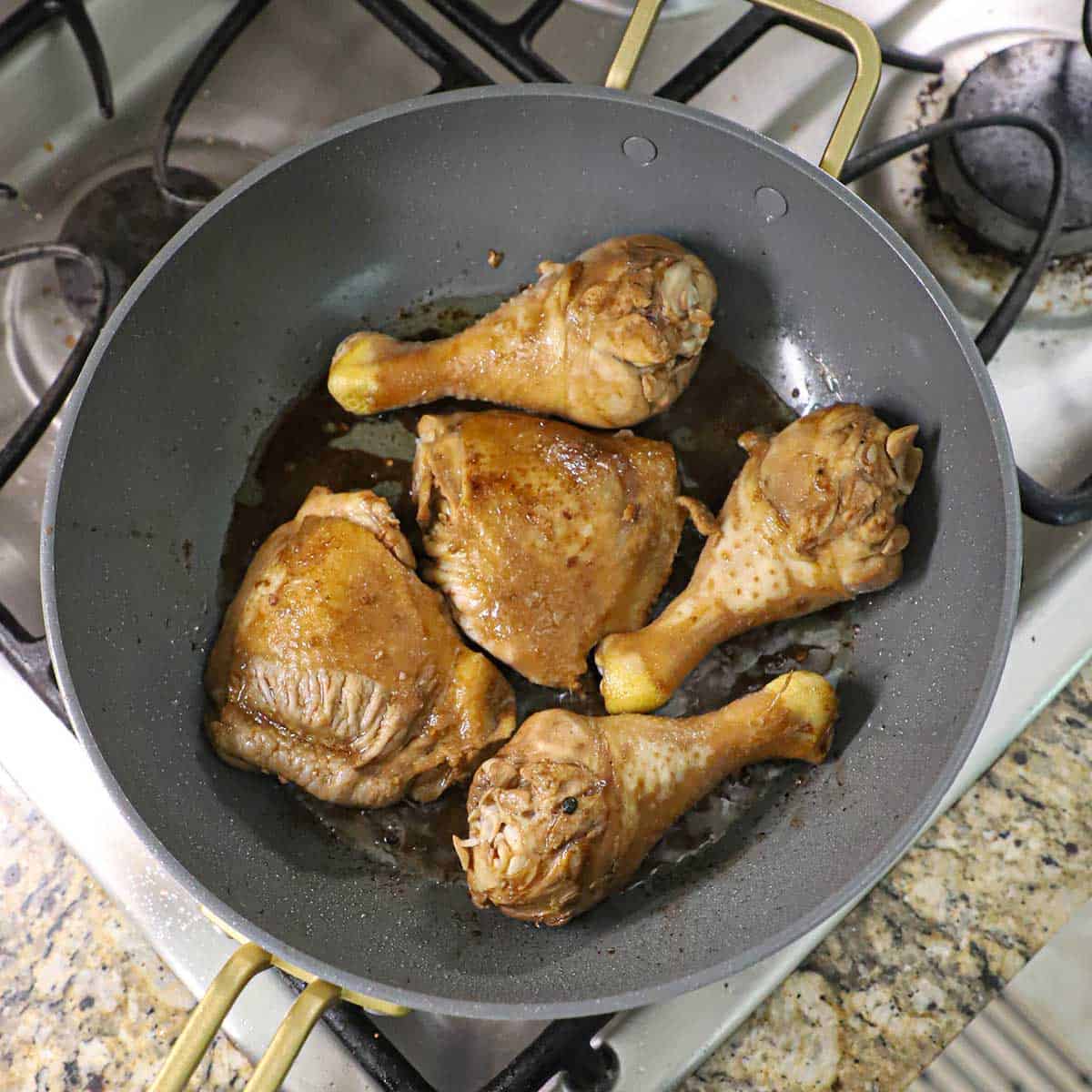 Marinated chicken thighs and legs being seared in a large non-stick skillet on a gas stove.