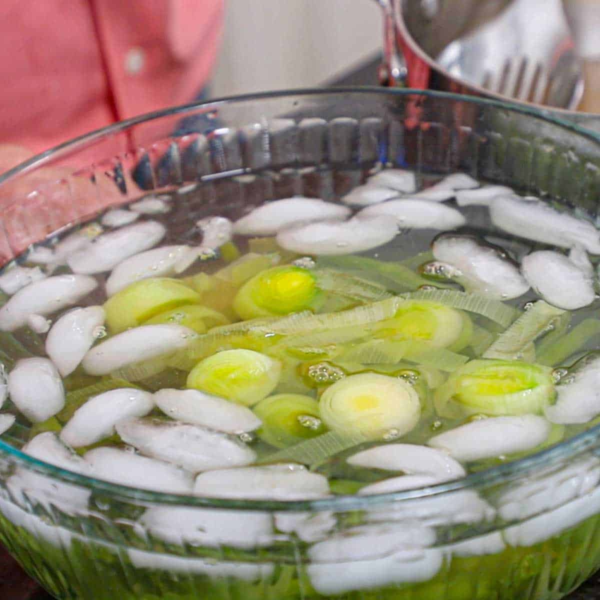 A large glass bowl filled with sliced leeks sitting on a black marble counter.