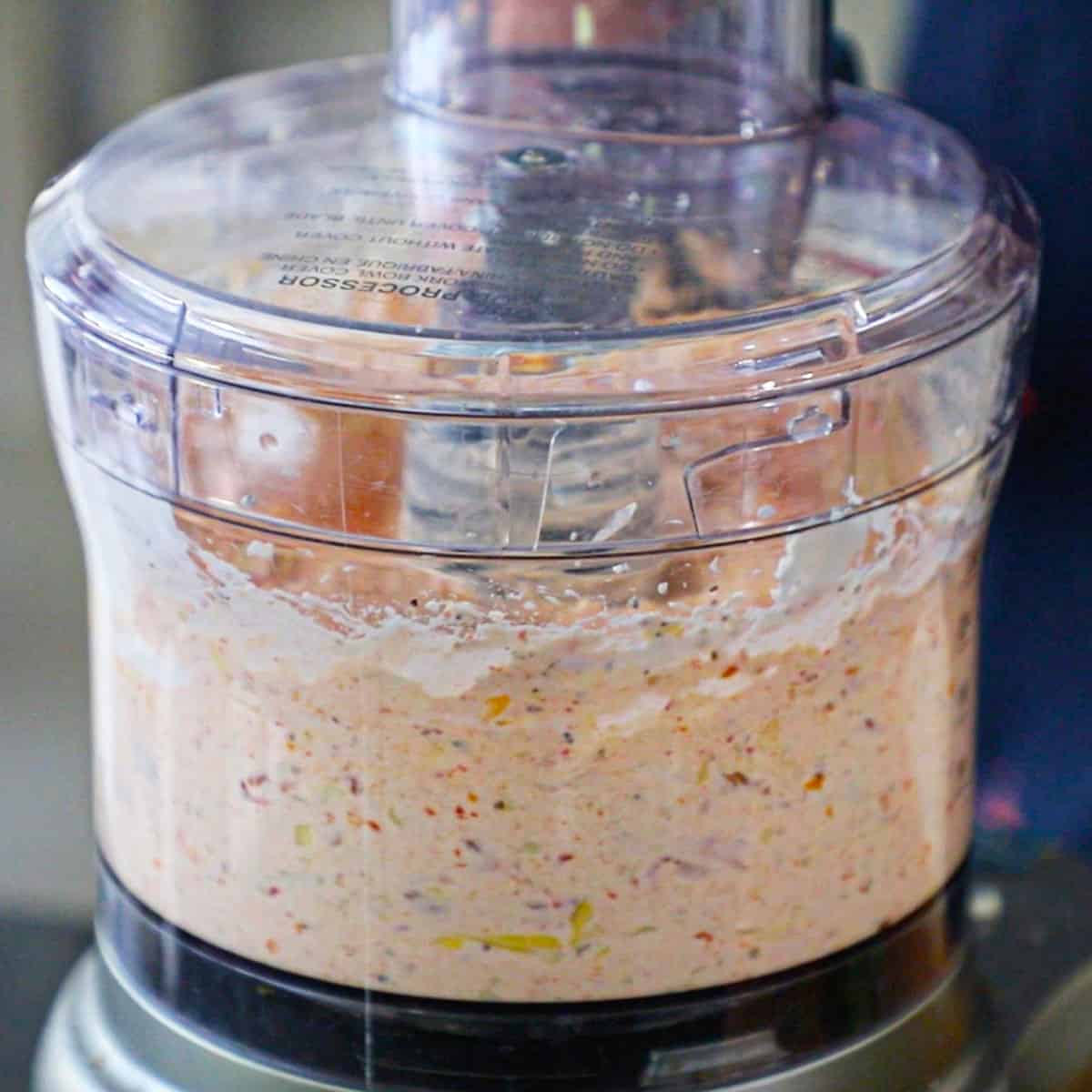 A close-up view of sun-dried tomato and artichoke dip that has been processed in a clear food processor.