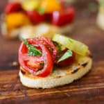 A single serving of Summer bruschetta with tomato and basil resting on a wooden cutting board.