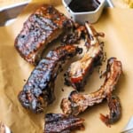 A small baking pan lined with brown paper and topped with balsamic glazed baby back ribs with a small bowl filled with the glaze nearby.