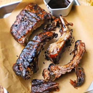 A small baking pan lined with brown paper and topped with balsamic glazed baby back ribs with a small bowl filled with the glaze nearby.