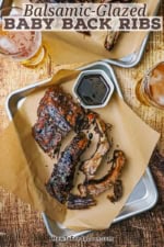 An overhead view of individual pieces of balsamic-glazed baby back ribs on brown paper on a metal tray.