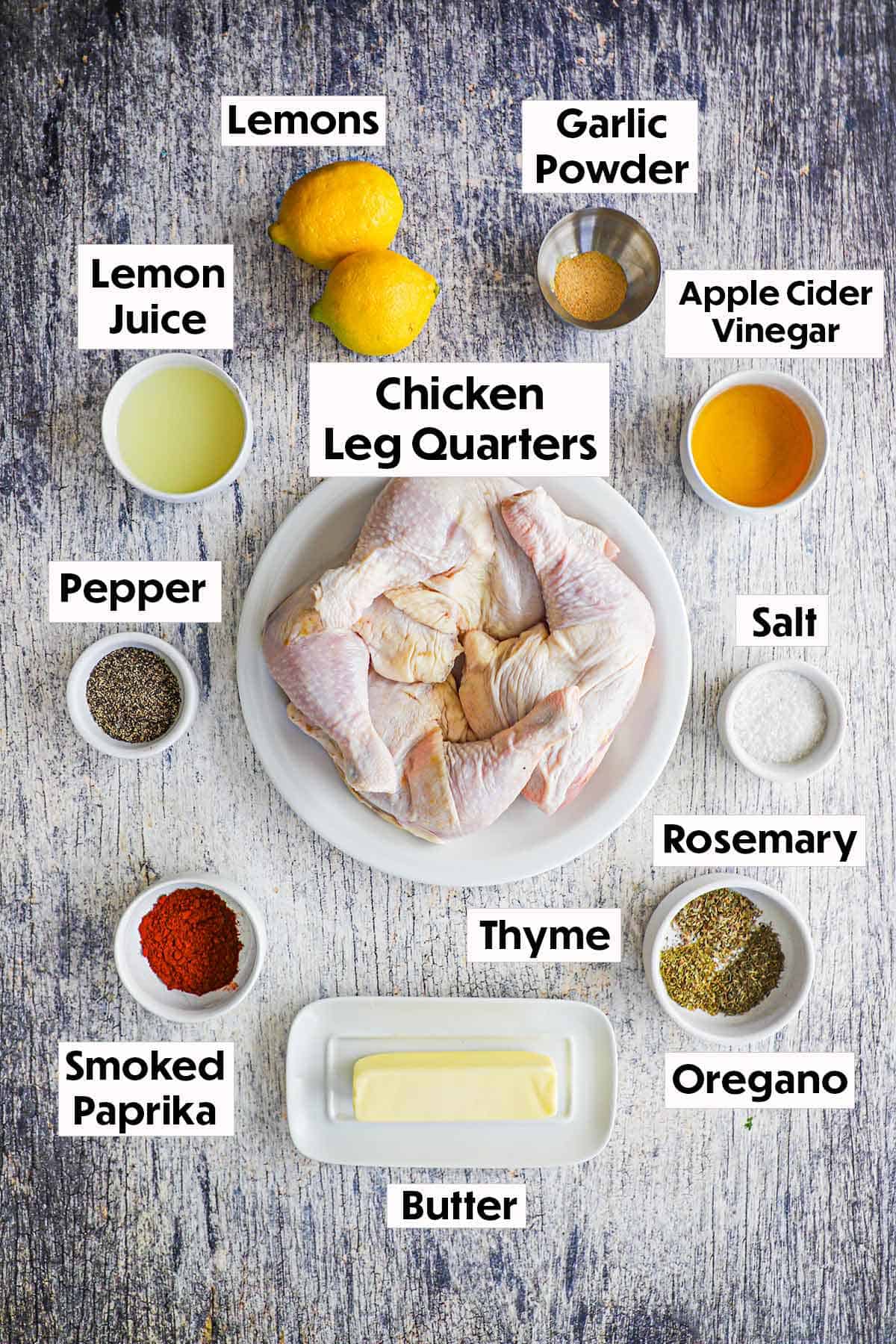 An arrangement of ingredients for best grilled chicken on a grey wooden background including raw chicken leg quarters, lemons, vinegar, lemon juice, butter, and seasonings.