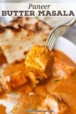A person using a fork to lift up a cubed piece of Indian panner over a bowl filled with paneer butter masala.