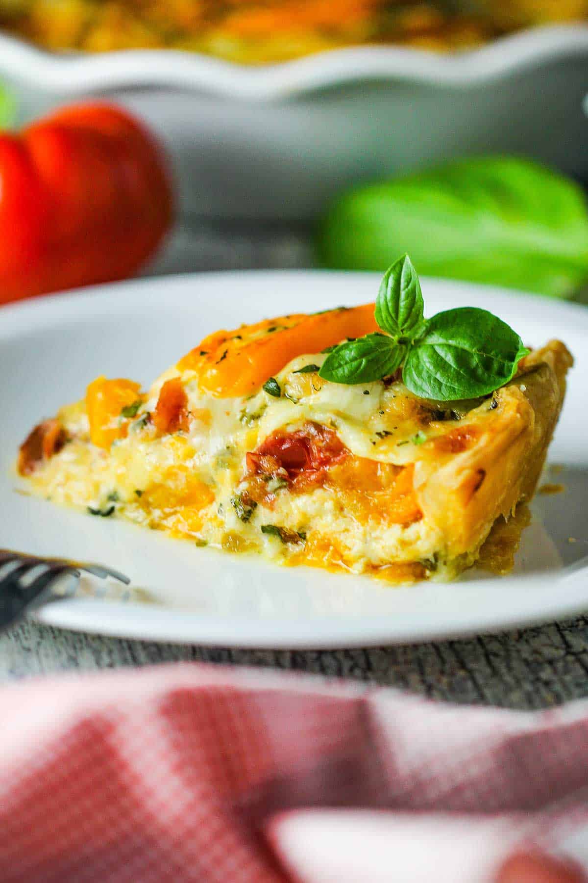 A slice of Southern tomato pie with a sprig of fresh basil on top all resting on a white dessert plate.