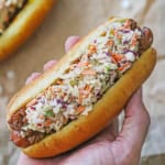 A person holding a West Virginia Slaw Dog in the palm of his hand over another slaw dog that is resting on a crumpled piece of brown paper.
