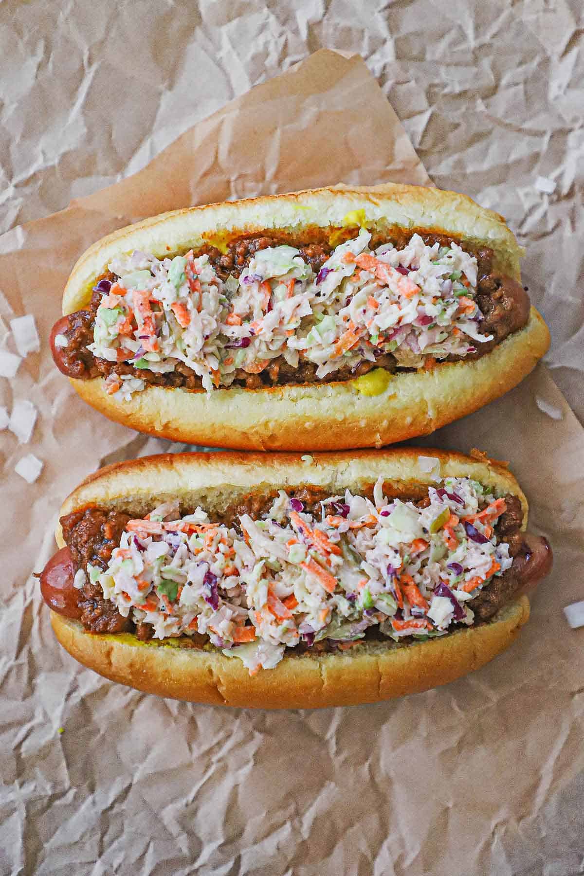 An overhead view of two fully loaded West Virginia Slaw Dogs resting side by side on a couple of pieces of crumpled brown paper.