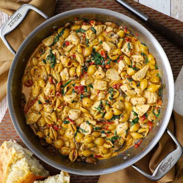 An overhead view of a large filled with One-Pot Marry Me Chicken Pasta including cooked pasta shells, bites of chicken, sun-dried tomatoes, wilted spinach, all in a creamy Tuscan sauce.