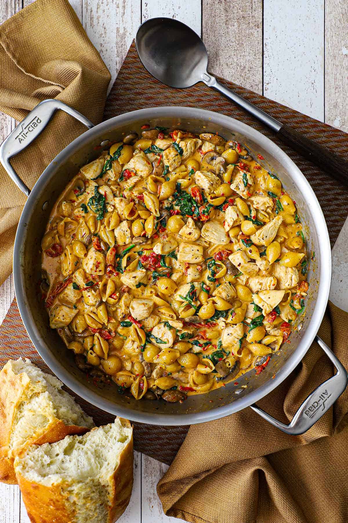 An overhead view of a large filled with One-Pot Marry Me Chicken Pasta including cooked pasta shells, bites of chicken, sun-dried tomatoes, wilted spinach, all in a creamy Tuscan sauce.