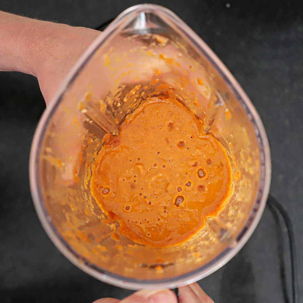 An overhead view of the inside of a blender that is filled with a butter masala gravy that was recently puréed.