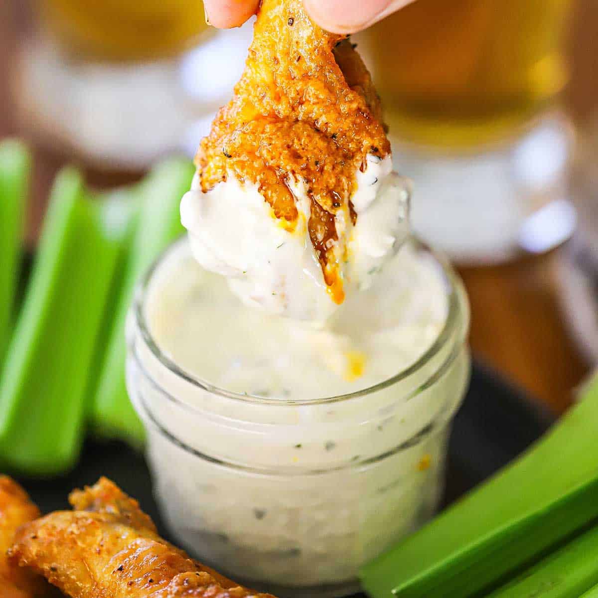A person lifting a buffalo chicken wing out of small jar filled with homemade blue cheese dressing.