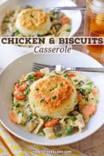 A white bowl filled with an untouched serving of chicken and biscuits with a glass of iced tea just behind the bowl.