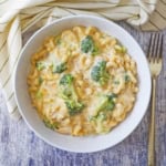 An overhead view of a white bowl filled with a serving of creamy mac and cheese with chicken and broccoli with a gold fork sitting next to the bowl.