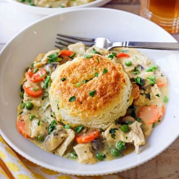 A white bowl filled with an untouched serving of chicken and biscuits with a glass of iced tea just behind the bowl.