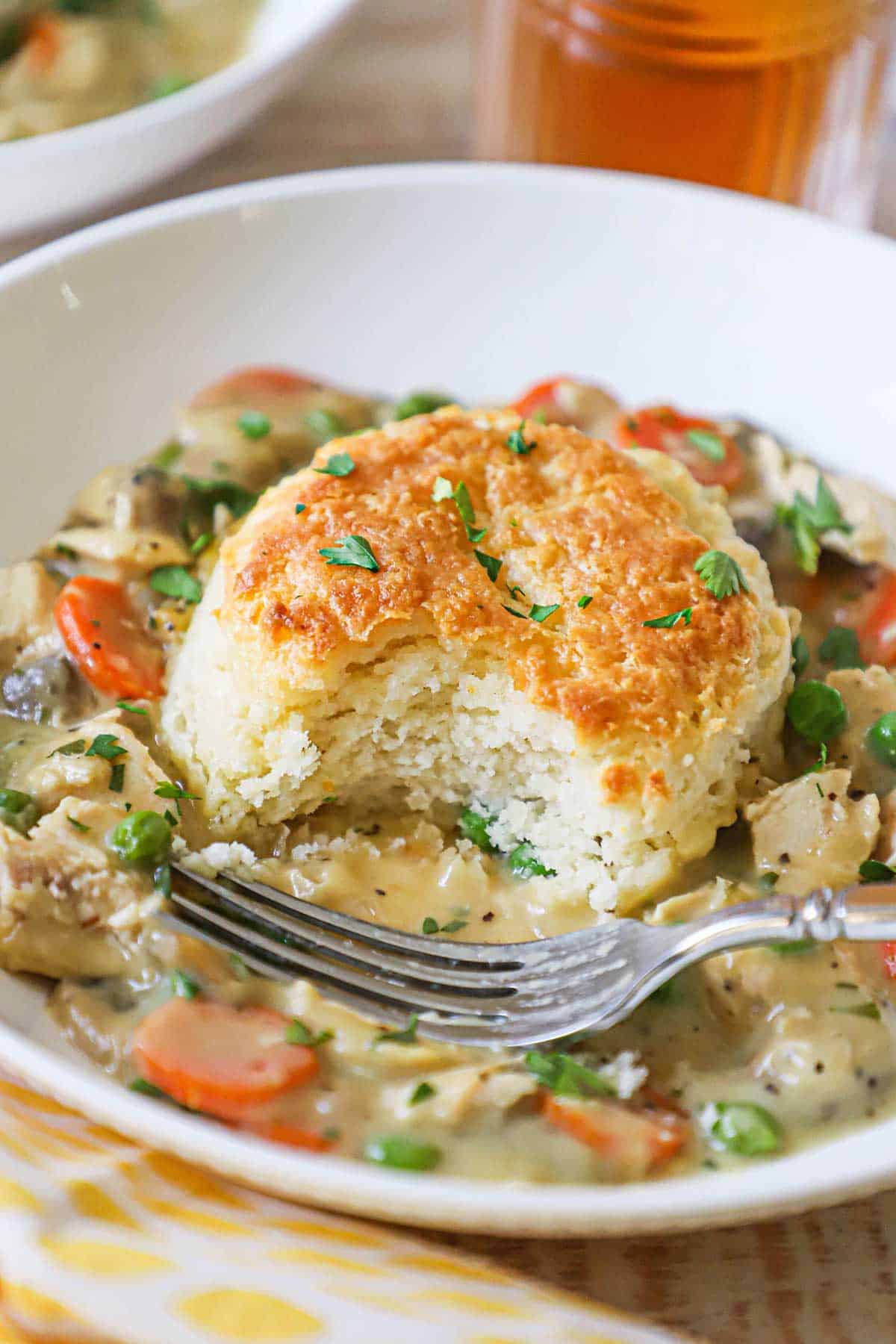 A half-eaten biscuit from a white bowl filled with a serving of chicken and biscuits casserole with a fork resting in the bowl.
