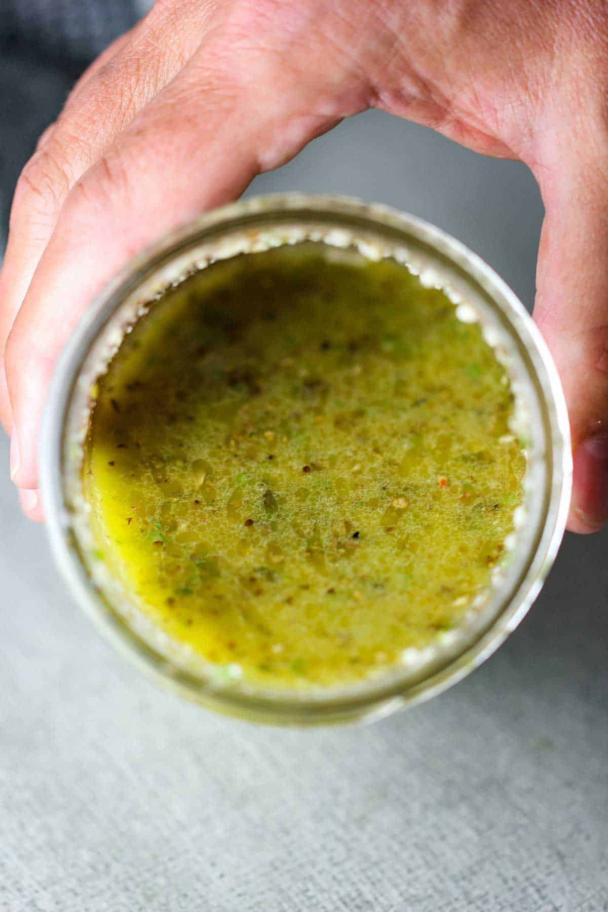 A person holding a jar filled with homemade Italian dressing and tilting it sideways so the contents of the jar are visible.