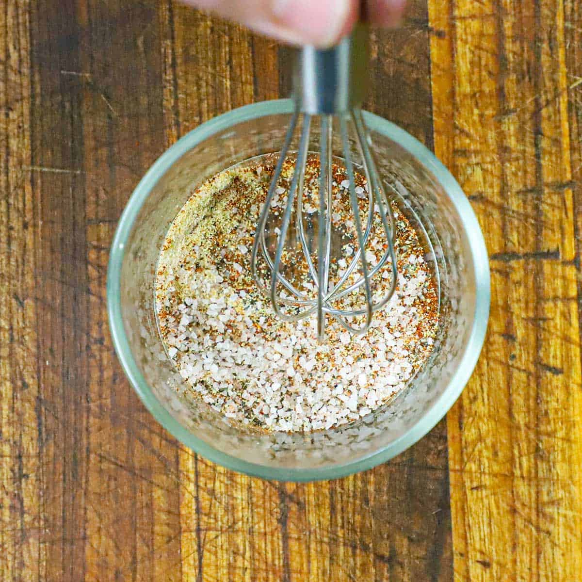 A person using a small whisk to combine the seasonings in a small bowl for Grilled Buffalo Shrimp.