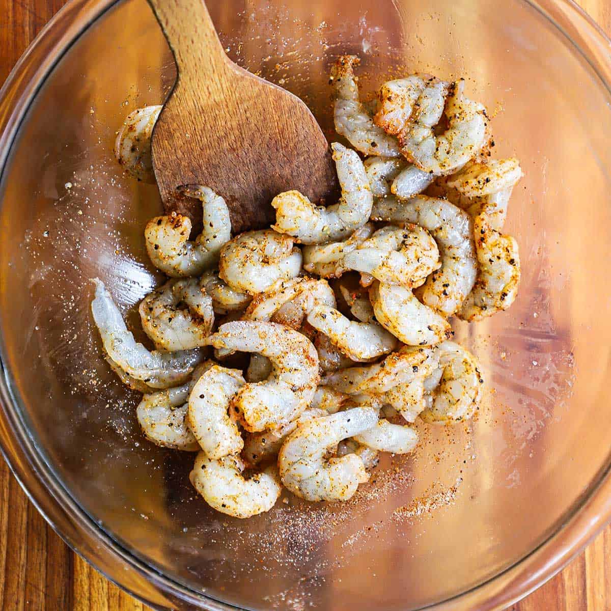 A large glass bowl filled with uncooked shelled shrimp that has been tossed with chili powder and other seasonings.