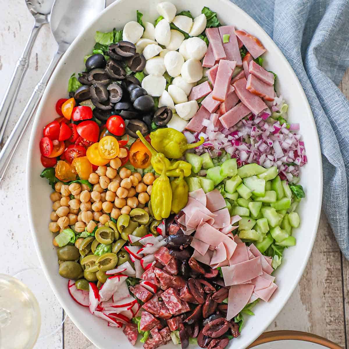 An overhead view of a large platter filled with piles of vegetables, cured meats, olives, mozzarella balls, garbanzo beans, and onions.